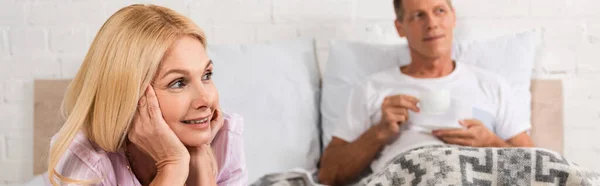 Mature couple on bed and man drinking coffee, panoramic shot — Stock Photo