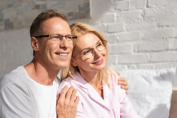 Sonriente hombre abrazando esposa en pijama en la cama por la mañana - foto de stock