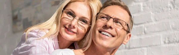 Panoramic shot of smiling couple in eyeglasses hugging at home — Stock Photo