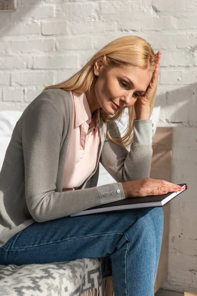 Thoughtful woman with notebook sitting on bed — Stock Photo