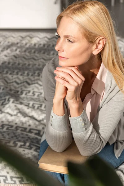 Nachdenkliche Frau mit Buch auf Knien im Bett — Stockfoto