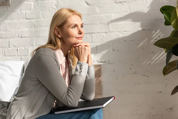 Side view of woman with notebook at knees sitting on bed — Stock Photo