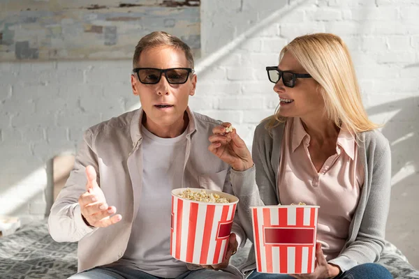 Pareja madura en gafas 3d sosteniendo cubos con palomitas de maíz en la cama - foto de stock