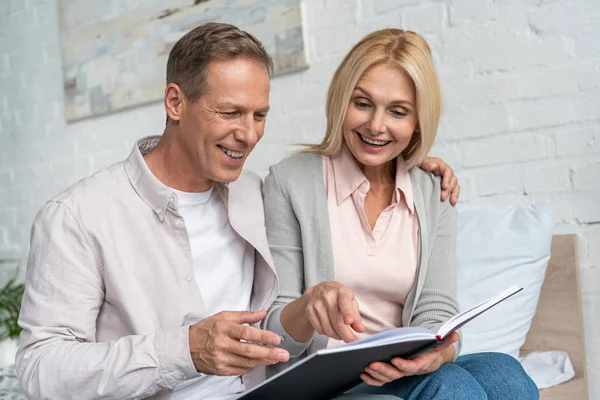 Lächelndes Paar blickt auf Notizbuch, während es auf dem Bett sitzt — Stockfoto