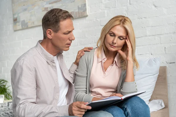 Man calming down thoughtful wife with notebook on bed — Stock Photo
