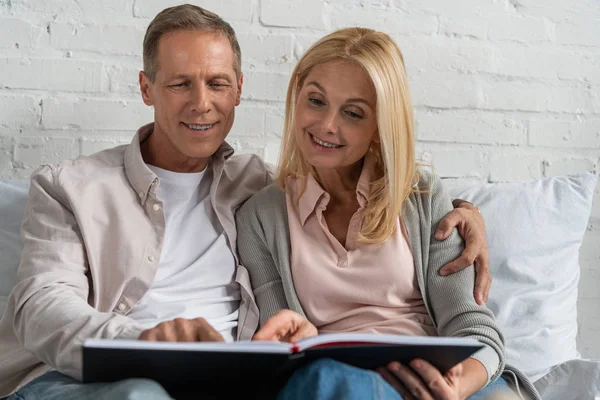 Lächelndes Paar blickt auf Notizbuch, während es auf dem Bett sitzt — Stockfoto