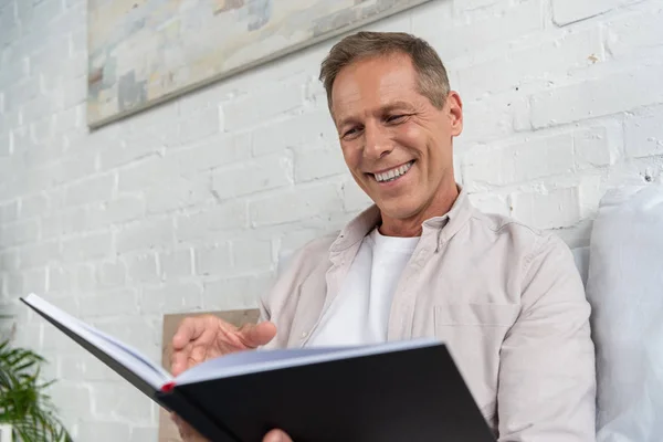 Lächelnder Mann blickt auf Notizbuch, während er auf dem Bett sitzt — Stockfoto