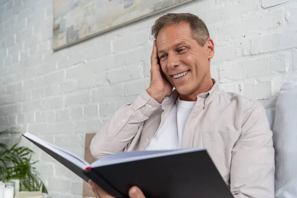 Aufgeregter Mann schaut in Notizbuch, während er auf dem Bett sitzt — Stockfoto