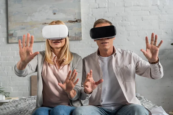 Пара в наушниках виртуальной реальности, играющая в видеоигры и жестикулирующая на кровати — стоковое фото