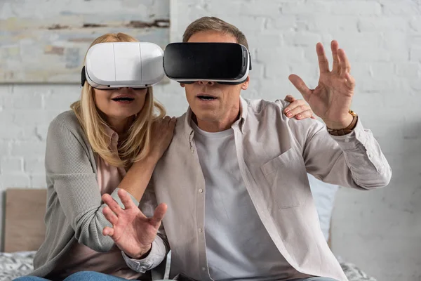 Пара в наушниках виртуальной реальности, играющая в видеоигры на кровати — стоковое фото