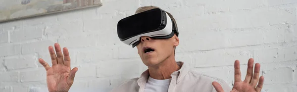 Panoramic shot of exited man in virtual reality headset at home — Stock Photo