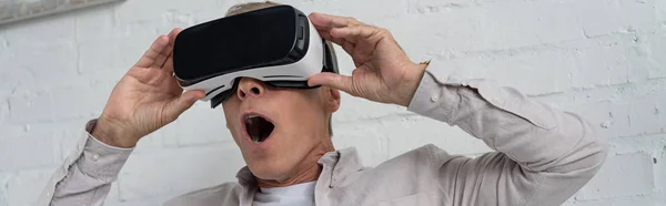 Hombre sorprendido en auriculares de realidad virtual jugando videojuego, tiro panorámico - foto de stock