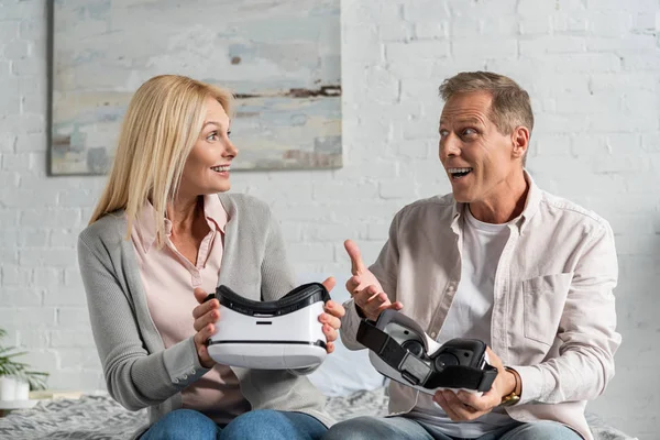 Exited couple holding virtual reality headsets on bed — Stock Photo