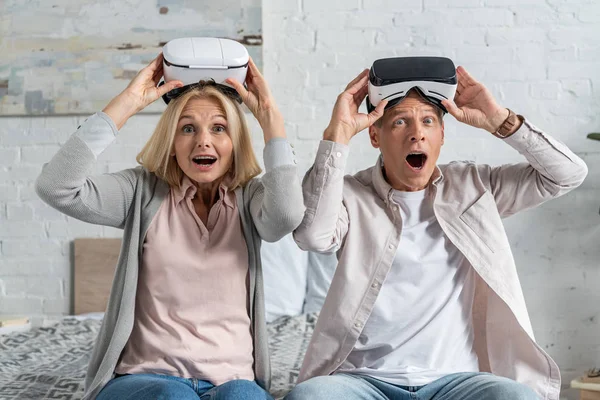 Shocked couple with virtual reality headsets looking at camera on bed — Stock Photo