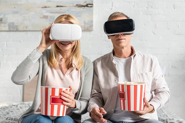 Coupe in virtual reality headsets holding popcorn on bed — Stock Photo