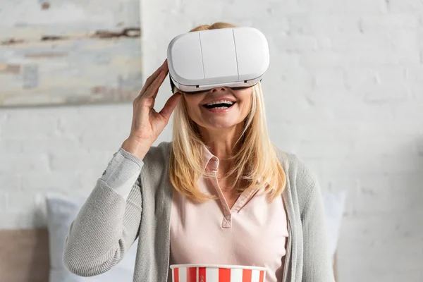 Екзистенціальна жінка в гарнітурі віртуальної реальності з попкорном на ліжку — стокове фото