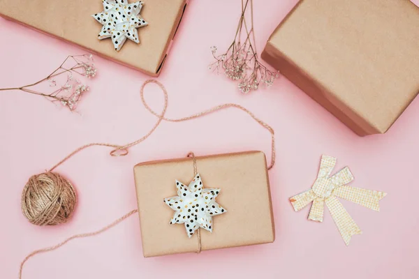 Vue du dessus des coffrets cadeaux de Noël artisanaux avec des fleurs et des arcs, isolés sur rose — Photo de stock