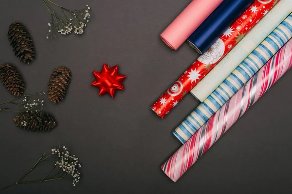 Top view of wrapping paper rolls, pine cones and flowers on black — Stock Photo