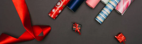 Panoramic shot of wrapping paper rolls and little gift boxes on black — Stock Photo