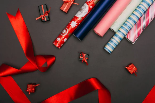 Vista superior de rollos de papel de embalaje, cinta y pequeñas cajas de regalo en negro - foto de stock