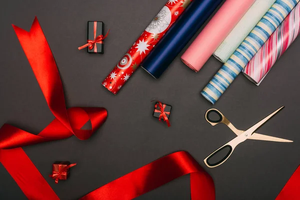 Top view of wrapping paper rolls, scissors and little gift boxes on black — Stock Photo
