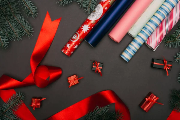 Top view of wrapping paper rolls, spruce branches and little gift boxes on black — Stock Photo