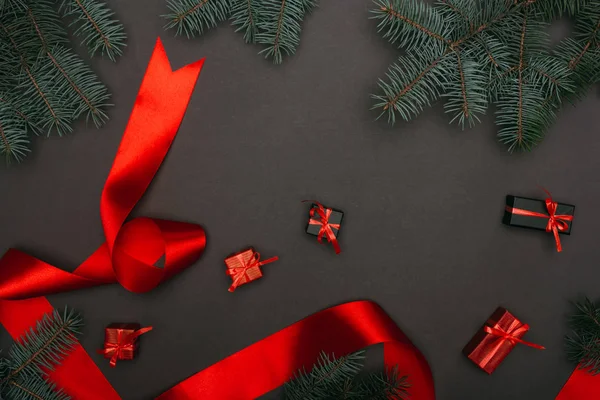 Top view of christmas gift boxes and red ribbon with spruce branches on black — Stock Photo