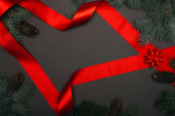 Top view of christmas red ribbon and spruce branches on black — Stock Photo