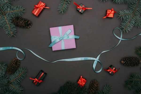 Top view of ribbon and christmas gift boxes with spruce branches and pine cones on black — Stock Photo