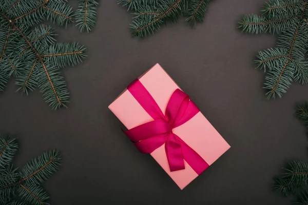 Vue du dessus du cadeau de Noël rose avec des branches d'épinette sur noir — Photo de stock