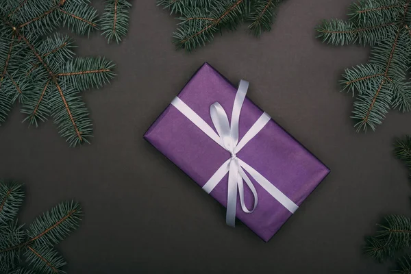 Top view of purple christmas gift with spruce branches on black — Stock Photo