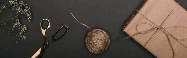 Panoramic shot of craft christmas gift with scissors, flowers and twine on black — Stock Photo