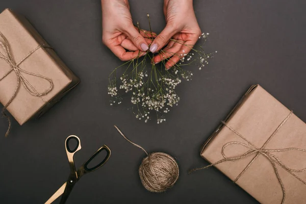 Cropped view of woman packing gift boxes with craft paper, twine and flowers on black — Stock Photo