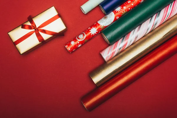 Vue du dessus des rouleaux de papier d'emballage et cadeau de Noël sur rouge — Photo de stock