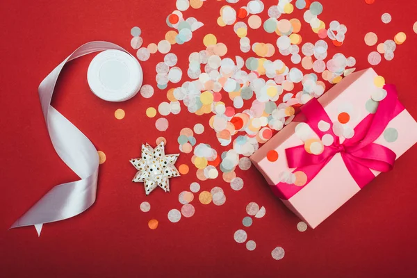 Vista superior de una navidad presente con lazo, cinta y confeti en rojo — Stock Photo