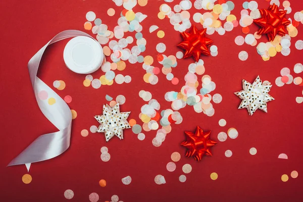 Vue du dessus des confettis de Noël, ruban blanc et noeuds sur rouge — Photo de stock