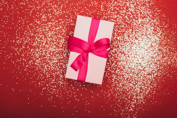 Top view of one christmas gift with golden confetti on red — Stock Photo