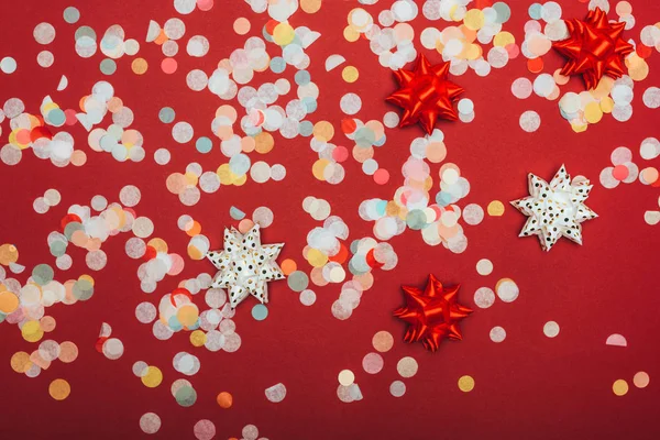 Сверху вид на рождественские конфетти и луки на красном — стоковое фото