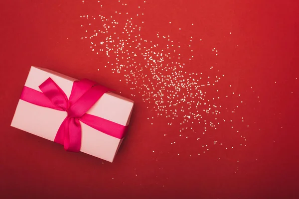 Top view of pink christmas present with golden confetti on red — Stock Photo