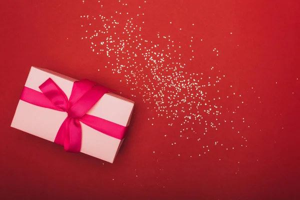 Vista dall'alto del regalo di Natale rosa con coriandoli dorati sul rosso — Foto stock