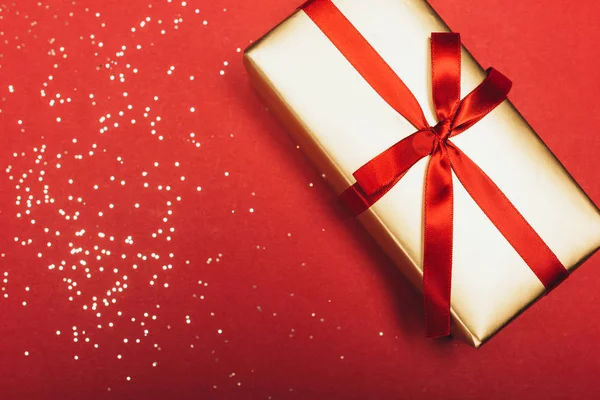 Один рождественский подарок с золотыми конфетти на красном — стоковое фото
