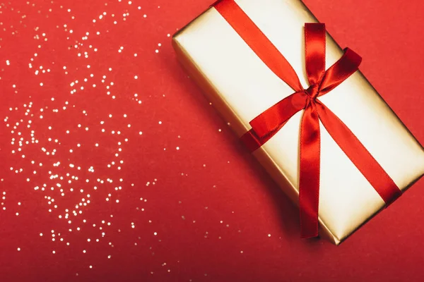Vista superior de un regalo de Navidad con confeti dorado sobre rojo — Stock Photo