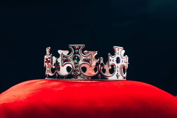 Ancient silver crown with gemstones on red pillow, isolated on black — Stock Photo