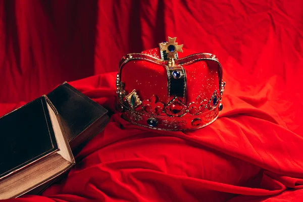 Стародавня золота корона з дорогоцінними каменями на червоній тканині з книгами — стокове фото