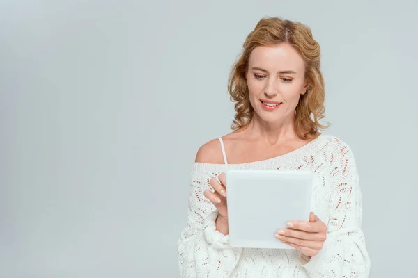 Attractive and smiling woman in sweater using digital tablet isolated on grey — Stock Photo