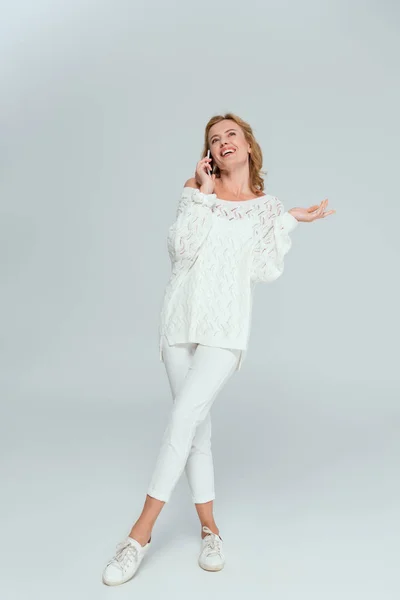 Mujer atractiva y sonriente hablando en el teléfono inteligente sobre fondo gris — Stock Photo