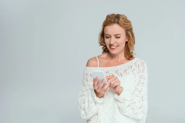 Mujer atractiva y sonriente usando teléfono inteligente aislado en gris - foto de stock