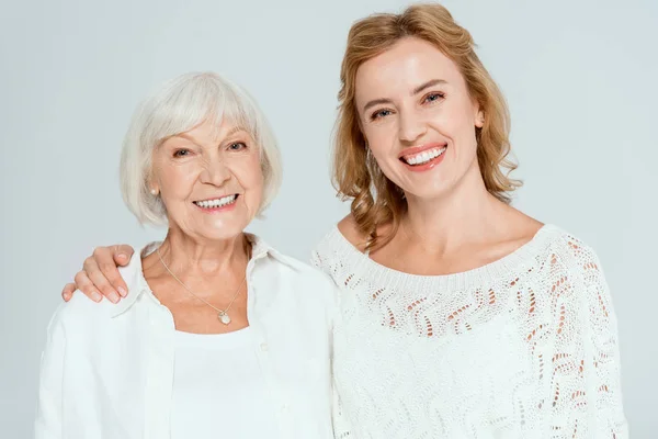 Smiling daughter hugging attractive mother and looking at camera isolated on grey — Stock Photo