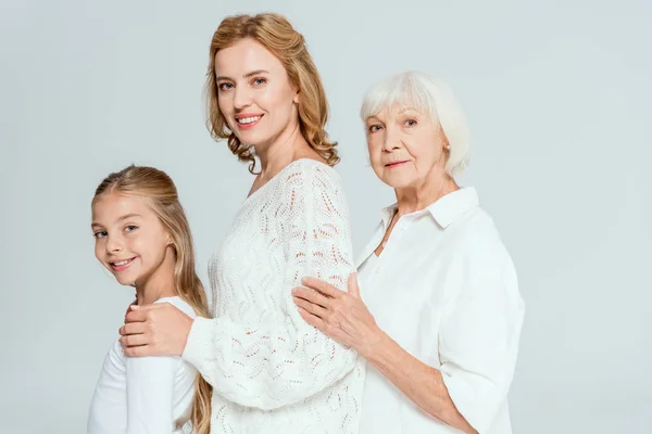 Smiling granddaughter, mother and grandmother hugging isolated on grey — Stock Photo