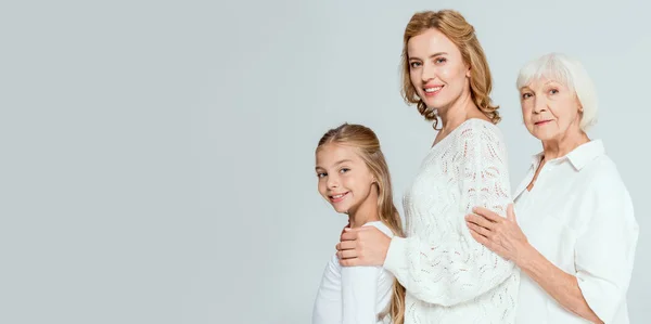 Panoramic shot of smiling granddaughter, mother and grandmother hugging isolated on grey — Stock Photo